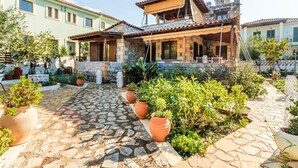 A courtyard with stone pathways, potted plants, and a building with a tiled roof and wooden pergola. - Mani s Garden Paradise - Elia Secluded Retreat (West Mani)