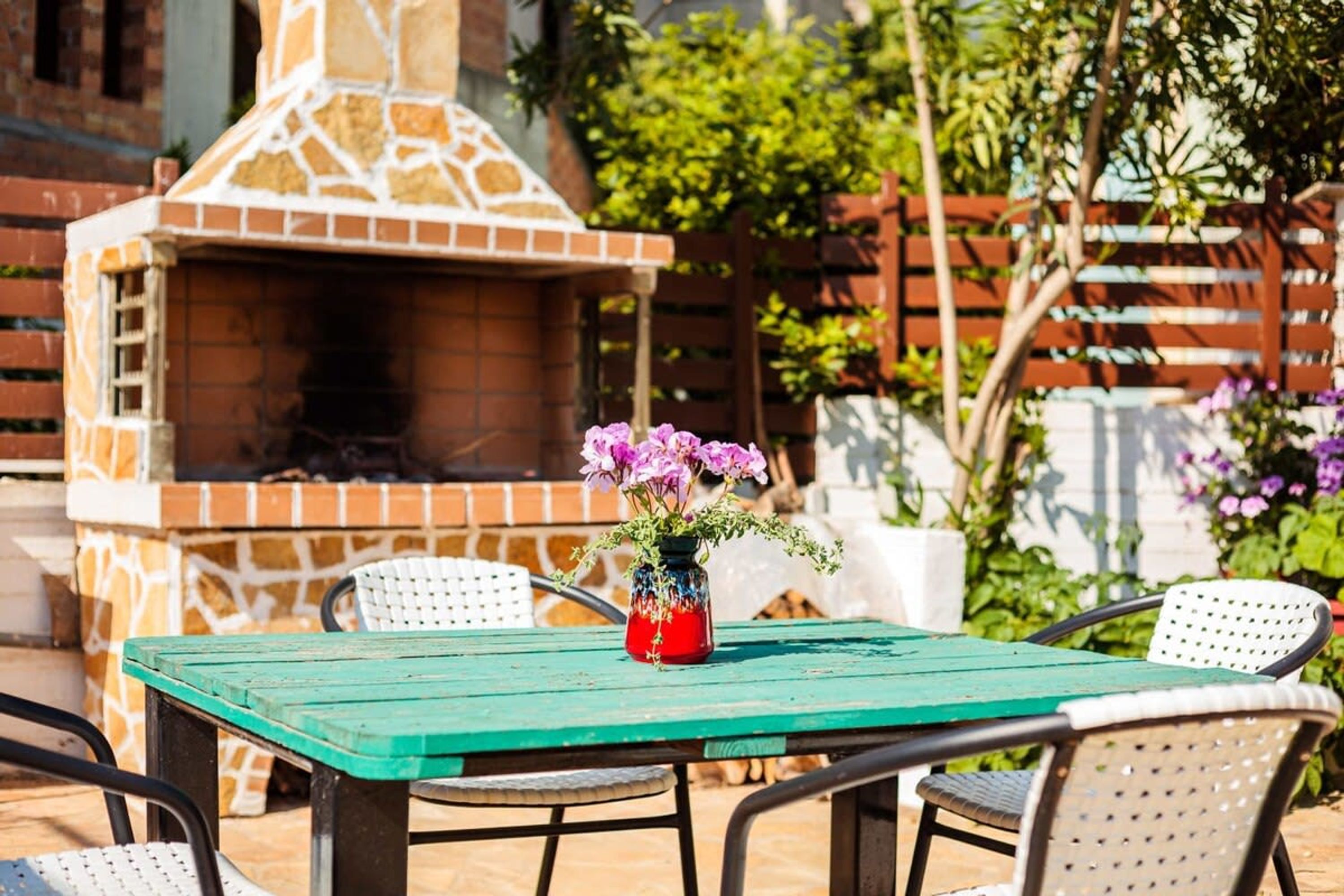 An outdoor patio with a brick oven, a green table, and white chairs.