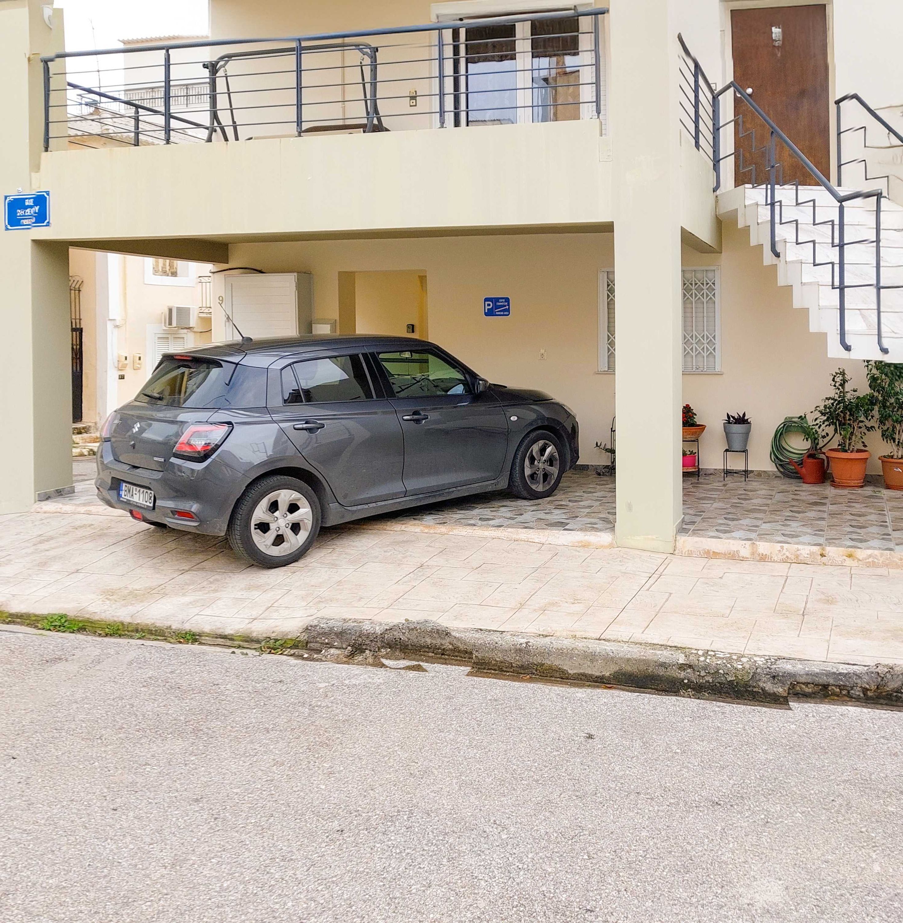 Ein grauer Kleinwagen steht in einer überdachten Tiefgarage, von wo aus eine Treppe zu einem Balkon im zweiten Stock führt.
