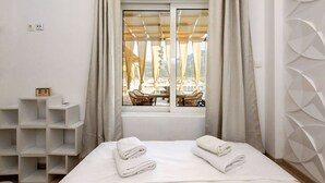 A hotel room with a bed, a window with curtains, a view of outdoor furniture, and a wall with a geometric pattern. - City Skyloft - Top Location Private Roof Garden (Kalamata)