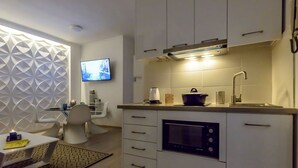 A modern kitchen with white cabinets, a built-in oven, and a flat-screen TV mounted on the wall. - City Skyloft - Top Location Private Roof Garden (Kalamata)