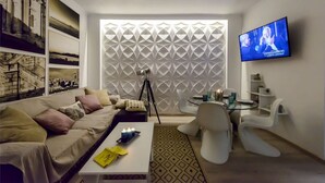 A modern living room with a sofa, a coffee table, a TV, and a patterned wall. - City Skyloft - Top Location Private Roof Garden (Kalamata)