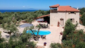A stone villa with a pool, outdoor seating, and a view of the sea.