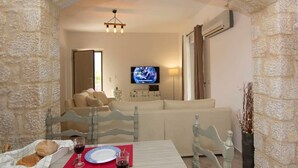 A cozy living room with a stone archway, a television, a sofa, and a dining table with a red placemat.