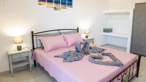 A neatly made bed with pink bedding, two bedside tables with lamps, a wall-mounted shelf, and a painting of a sunset over the ocean. - Atlantic Cave Haven-seaside Fully Equipped (Rhodes)
