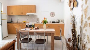 A modern kitchen with wooden cabinets, a dining table with chairs, and a decorative wall clock. - Atlantic Cave Haven-seaside Fully Equipped (Rhodes)