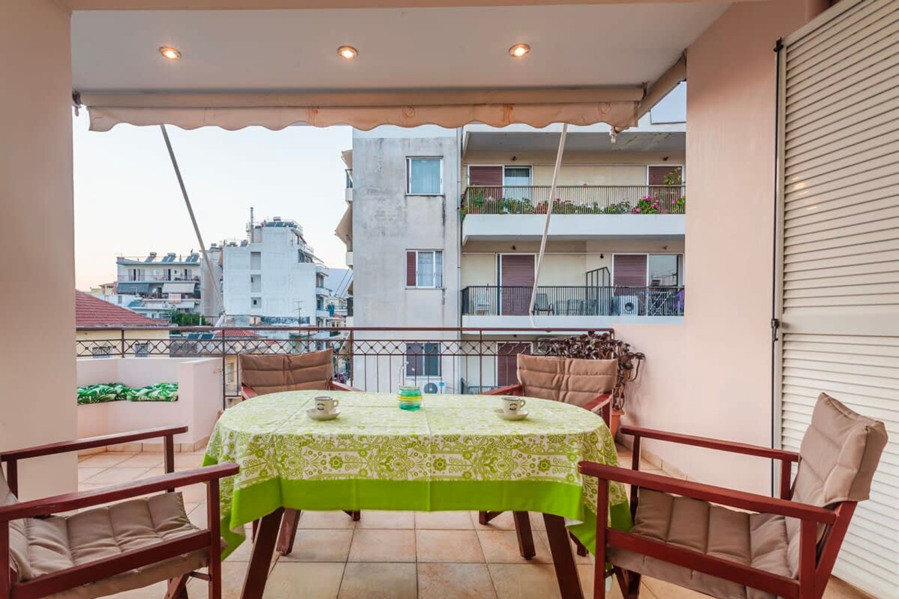 A balcony with a table set for two, chairs, and a view of neighboring buildings.