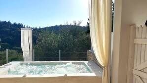 Un jacuzzi con un fondo de pared de piedra, una valla de madera y vistas a una colina boscosa.