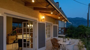 Eine offene Terrasse mit Tisch und Stühlen, eine Treppe, die zu einer erhöhten Ebene führt, und ein Blick auf Berge im Hintergrund.