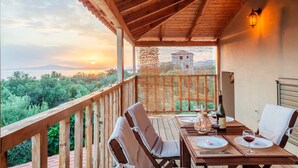 A wooden deck with a table set for two, overlooking a scenic view of mountains and a building. - Selinitsa Stone Studio - Mani Seaview Retreat (West Mani)