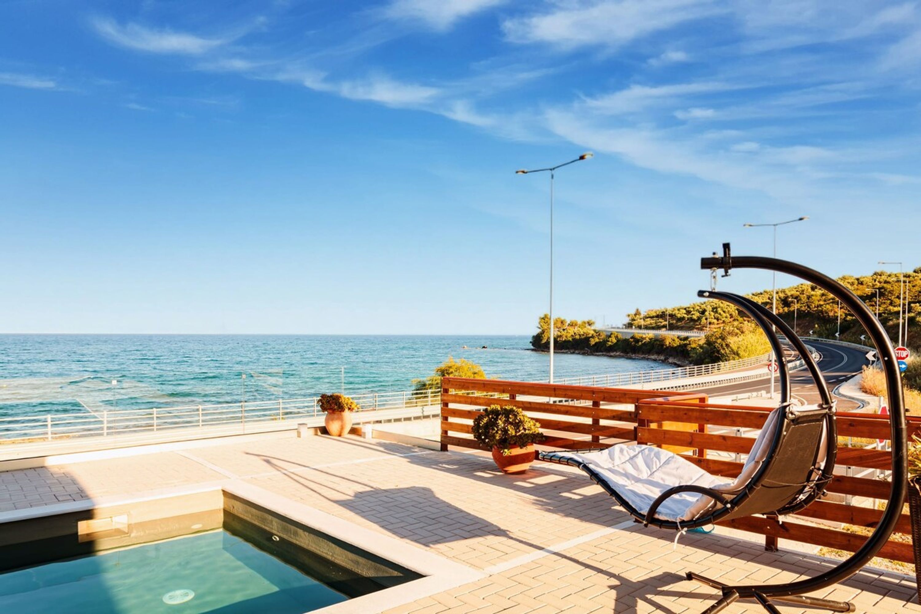 Un espace aménagé au bord de la piscine, avec un banc, un fauteuil suspendu et une vue sur la mer.