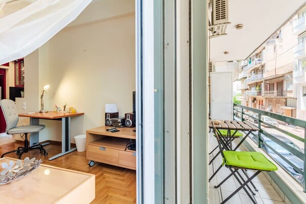 A modern apartment with a balcony, a wooden desk, a chair, a small table, and a sofa.