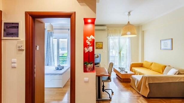 A modern living room with a sofa, a dining table, and a kitchen area visible through an open door. - Athens Strawberry Hideaway - City Chic Retreat (Athens)