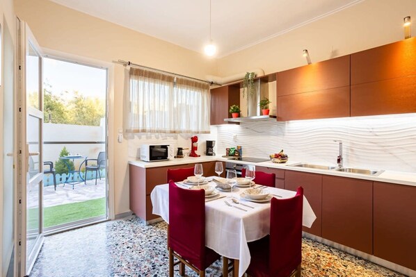 A modern kitchen with a dining area, featuring a large window, a microwave, a sink, and a dining table set for four. - Avia Seaview Getaway - Konstantina s Hidden Haven (West Mani)