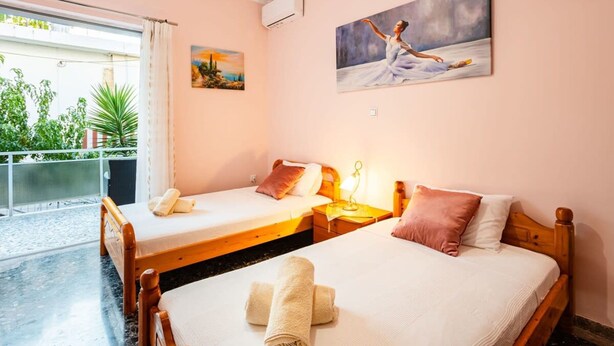 Habitación de hotel con dos camas individuales, un balcón con plantas y un cuadro en la pared.