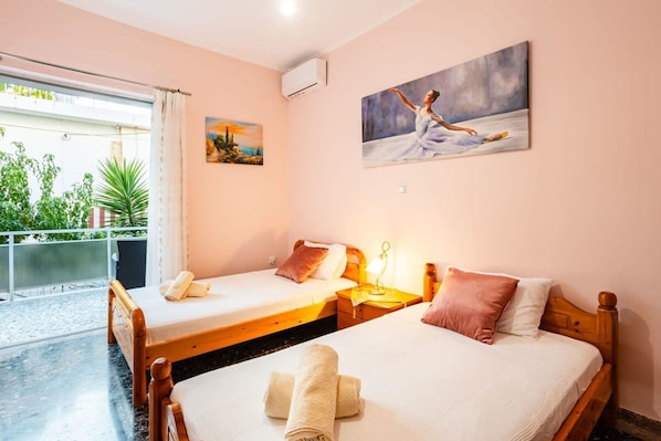 A hotel room with two single beds, a balcony with plants, and a painting on the wall.