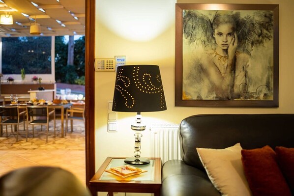 A living room with a black leather sofa, a table lamp, and a framed artwork on the wall. - Verga Sunset Gem - Ilia Seaview Private Retreat (Kalamata)