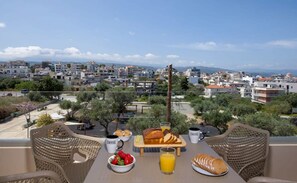 A balcony with wicker chairs, a table set with breakfast, and a view of a coastal town. - A Heaven View Park Hideaway - Chania Nest (Chania)