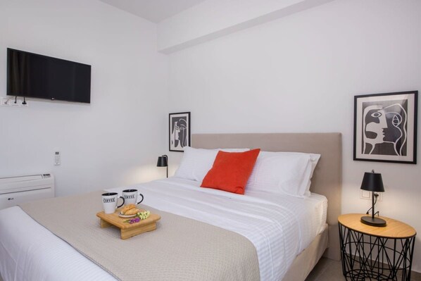 Une chambre d’hôtel comprenant un lit, un téléviseur fixé au mur, une table de chevet avec une lampe et des œuvres d’art accrochées aux murs.