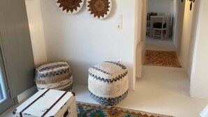 A hallway with two decorative wall-mounted items, a patterned rug, and a white table in the background. - Rustic Stone House in the Heart of Folegandros (Folegandros)