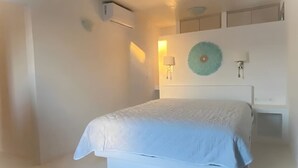 A bedroom with a bed, a wall-mounted air conditioner, a wall lamp, and a decorative wall piece. - Rustic Stone House in the Heart of Folegandros (Folegandros)