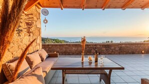 Una terraza con techo de madera, pared de piedra y vista al mar.