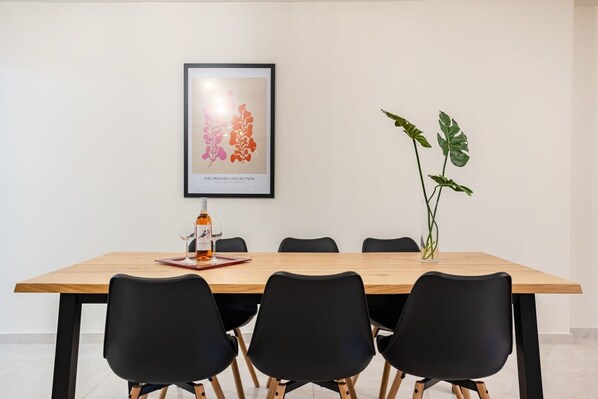 A dining area with a wooden table, black chairs, a framed artwork, and a potted plant. - Escape to Kalamata s Old City Your Urban Oasis (Kalamata)