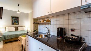 Une chambre d’hôtel compacte comprenant un coin cuisine, un lit avec une couverture verte, une table de chevet et un tableau au mur.
