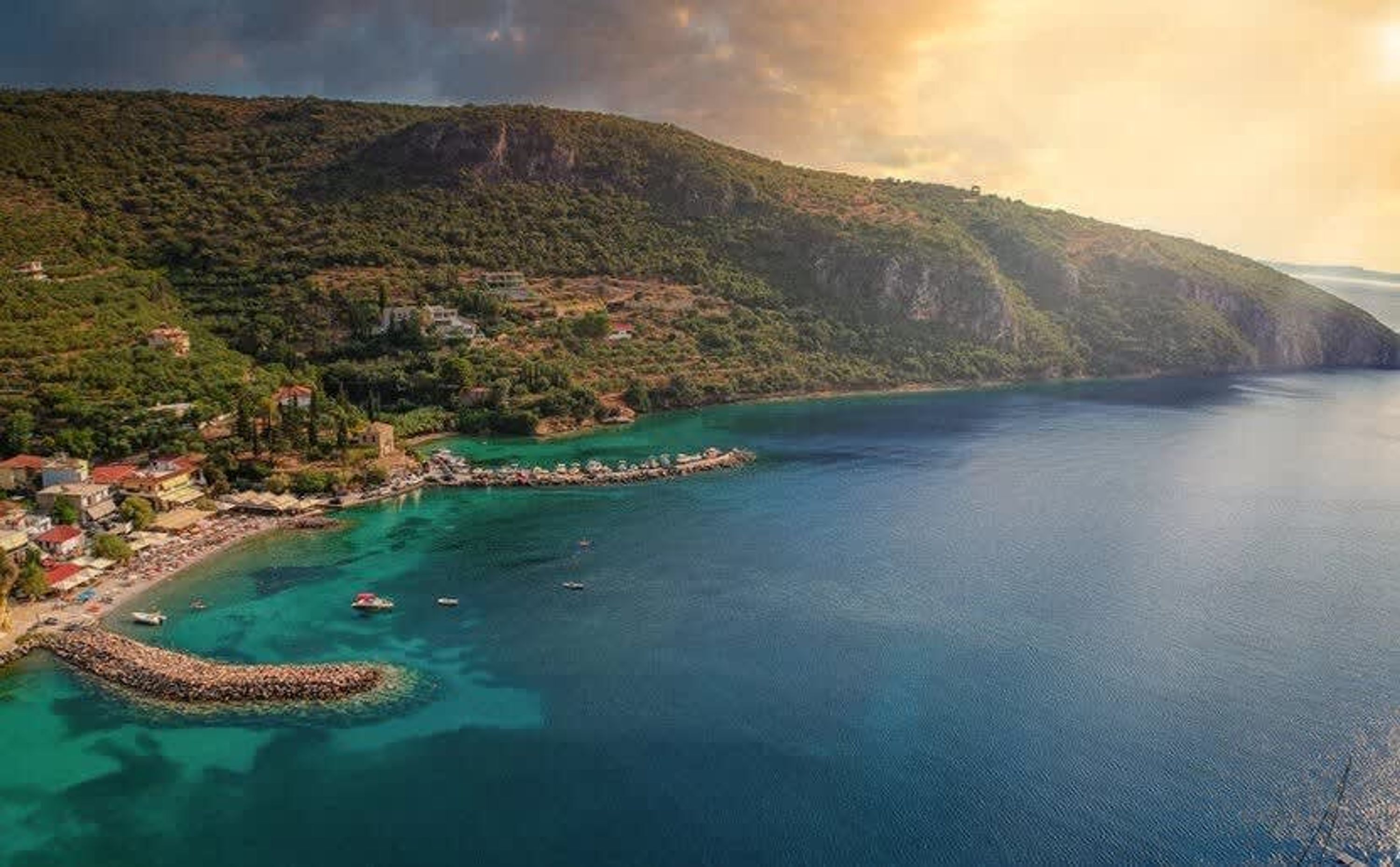 Vista aérea de una zona costera con mar azul cristalino, un litoral rocoso y un paisaje montañoso con edificios.