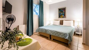Une chambre à coucher avec un lit, un bureau avec un ventilateur, une plante et une fenêtre avec des rideaux.