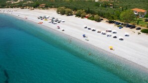 Una vista aerea di una spiaggia con acque turchesi cristalline, sabbia bianca e numerosi ombrelloni.