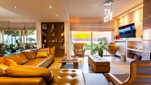 A modern living room with a sofa, ottoman, and armchair, a television, and a bookshelf. - Sunset Paradise - Verga s Ultimate Seaview Getaway (Kalamata)