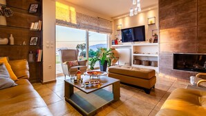 A modern living room with a sofa, coffee table, and TV. There is a fireplace and a bookshelf with decorative items. - Sunset Paradise - Verga s Ultimate Seaview Getaway (Kalamata)