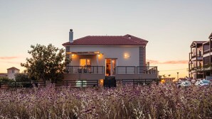A two-story house with a balcony, surrounded by a field of purple flowers, and adjacent to a multi-story building. - Navarino Captains Villa - Lux Private Pool Retreat (Trifylia)