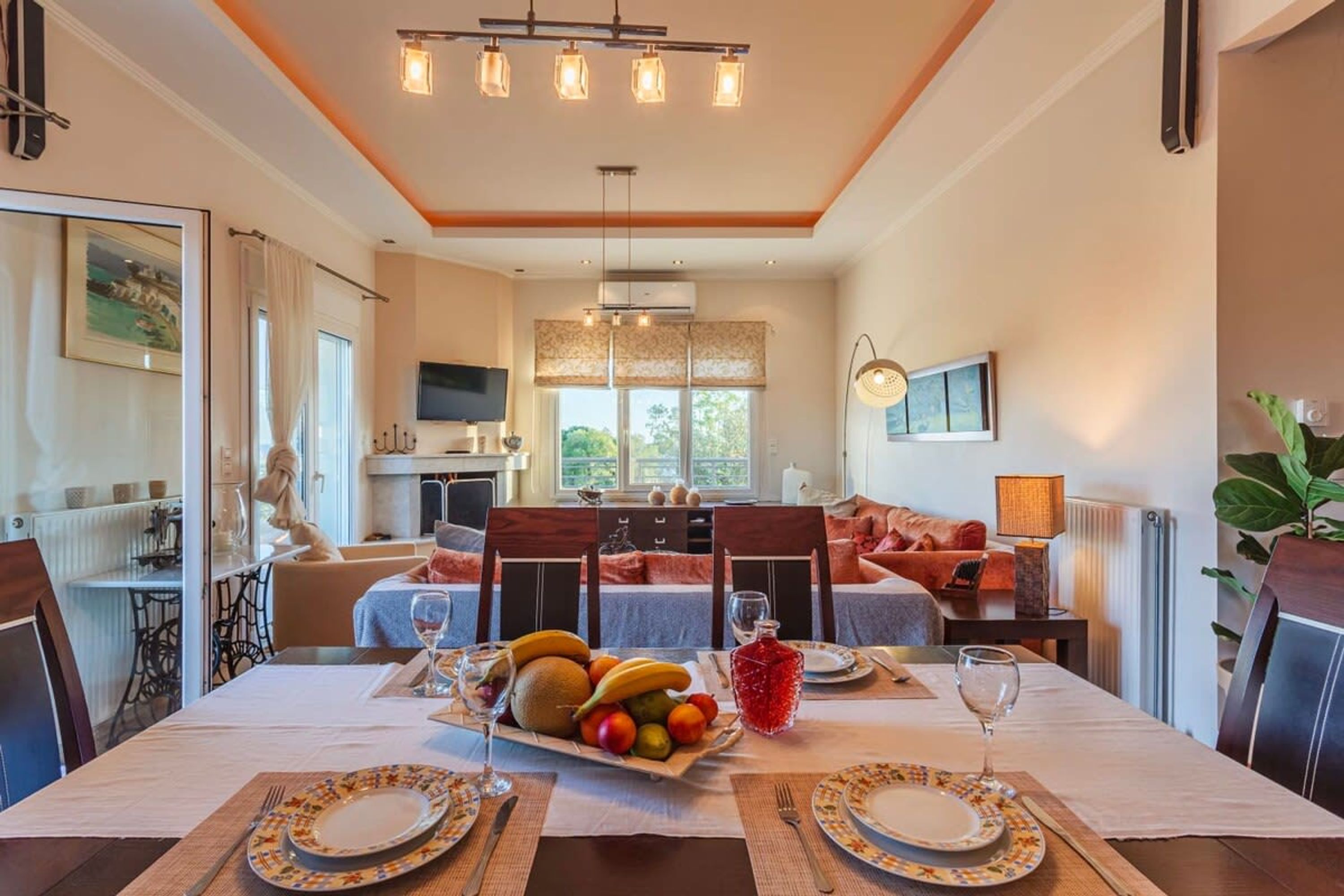 Un comedor con una mesa dispuesta para dos personas, un plato de fruta y una bebida roja.