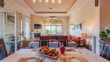 Un comedor con una mesa dispuesta para dos personas, un plato de fruta y una bebida roja.