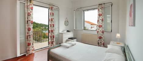 Una camera da letto con un letto, un comodino, una cassettiera, una finestra vista e un balcone con tende.