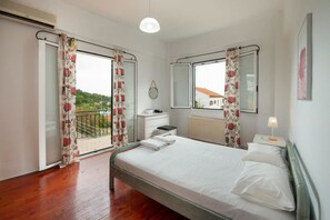 Une chambre à coucher comprenant un lit, une table de chevet, une commode, une fenêtre avec vue et un balcon avec des rideaux.