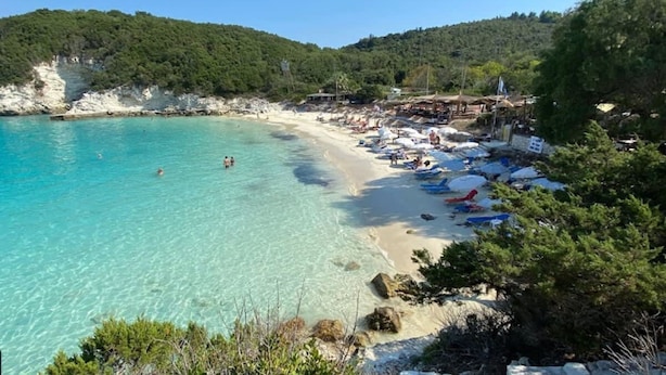 Una playa con agua turquesa cristalina, una orilla de arena y colinas verdes al fondo.