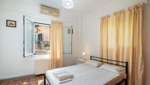 Un dormitorio con cama, mesita de noche, ventana con cortinas y radiador.