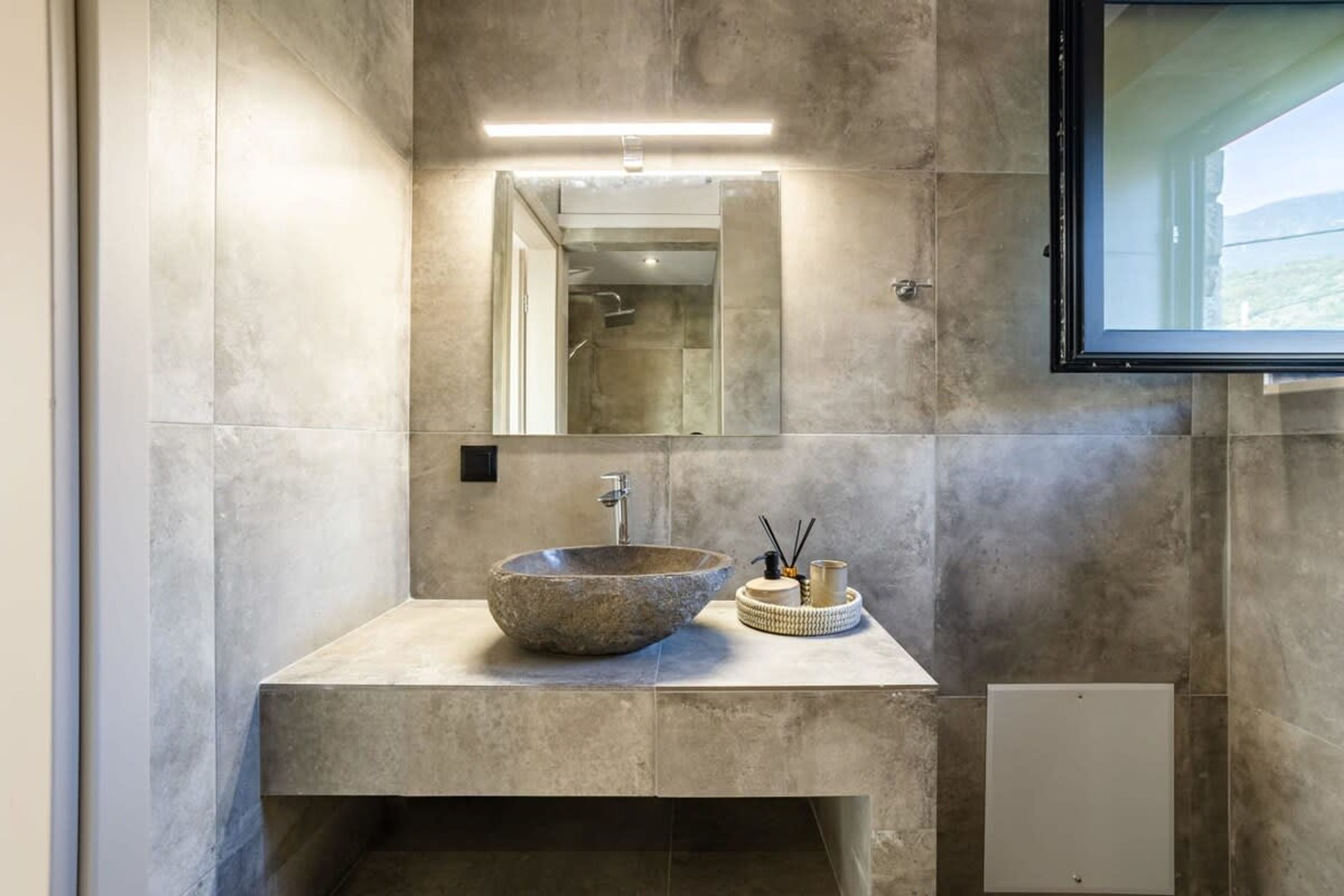 A modern bathroom with a large stone sink, a mirror, and a built-in shower.