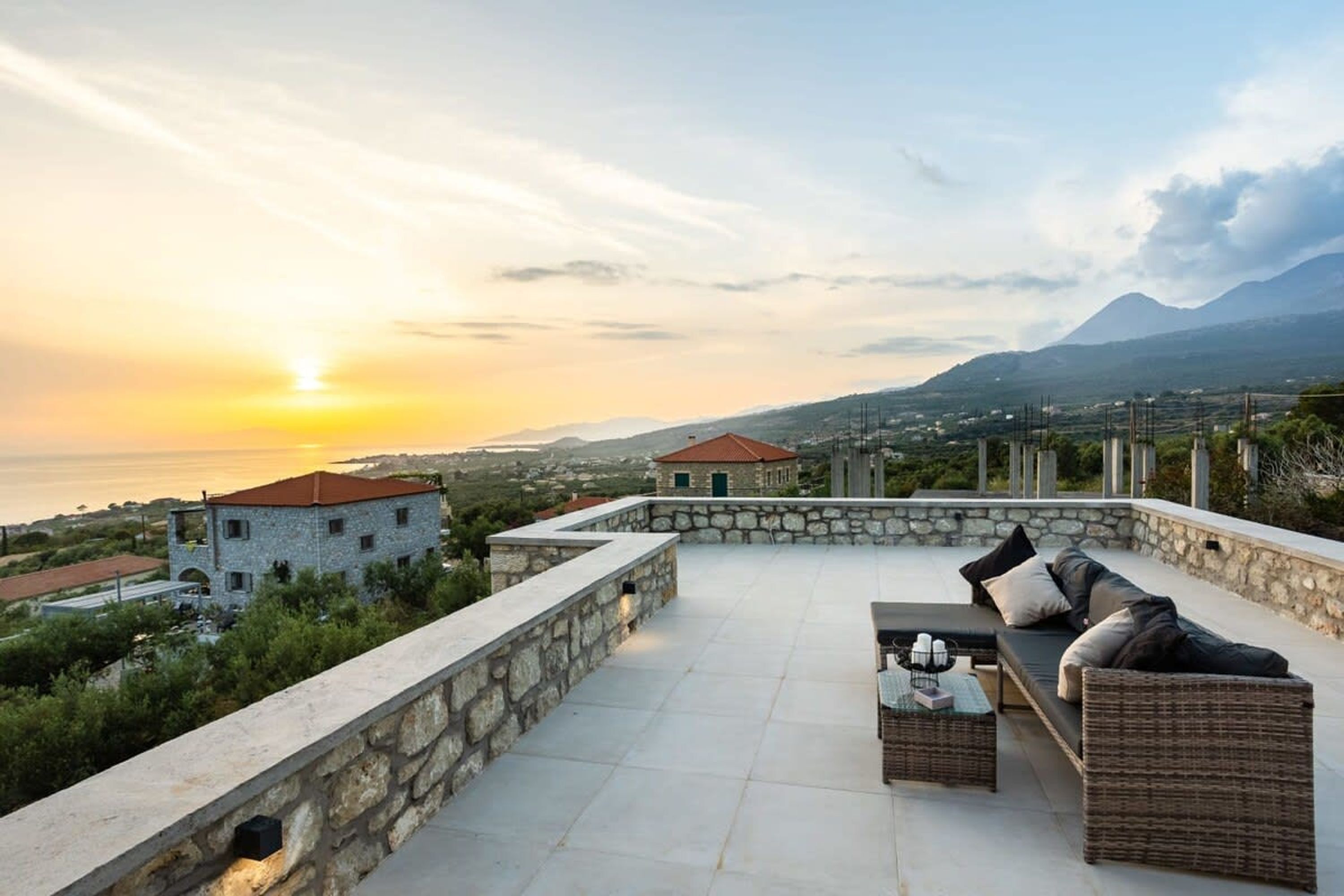 A rooftop terrace with a stone wall, a wicker sofa, and a table.