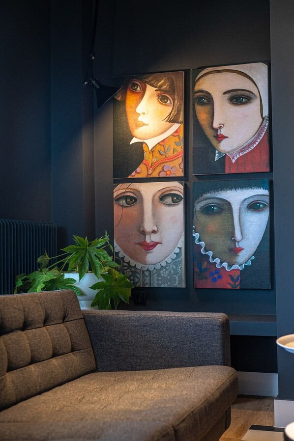 A room with a dark-colored sofa, a potted plant, and four paintings on the wall.