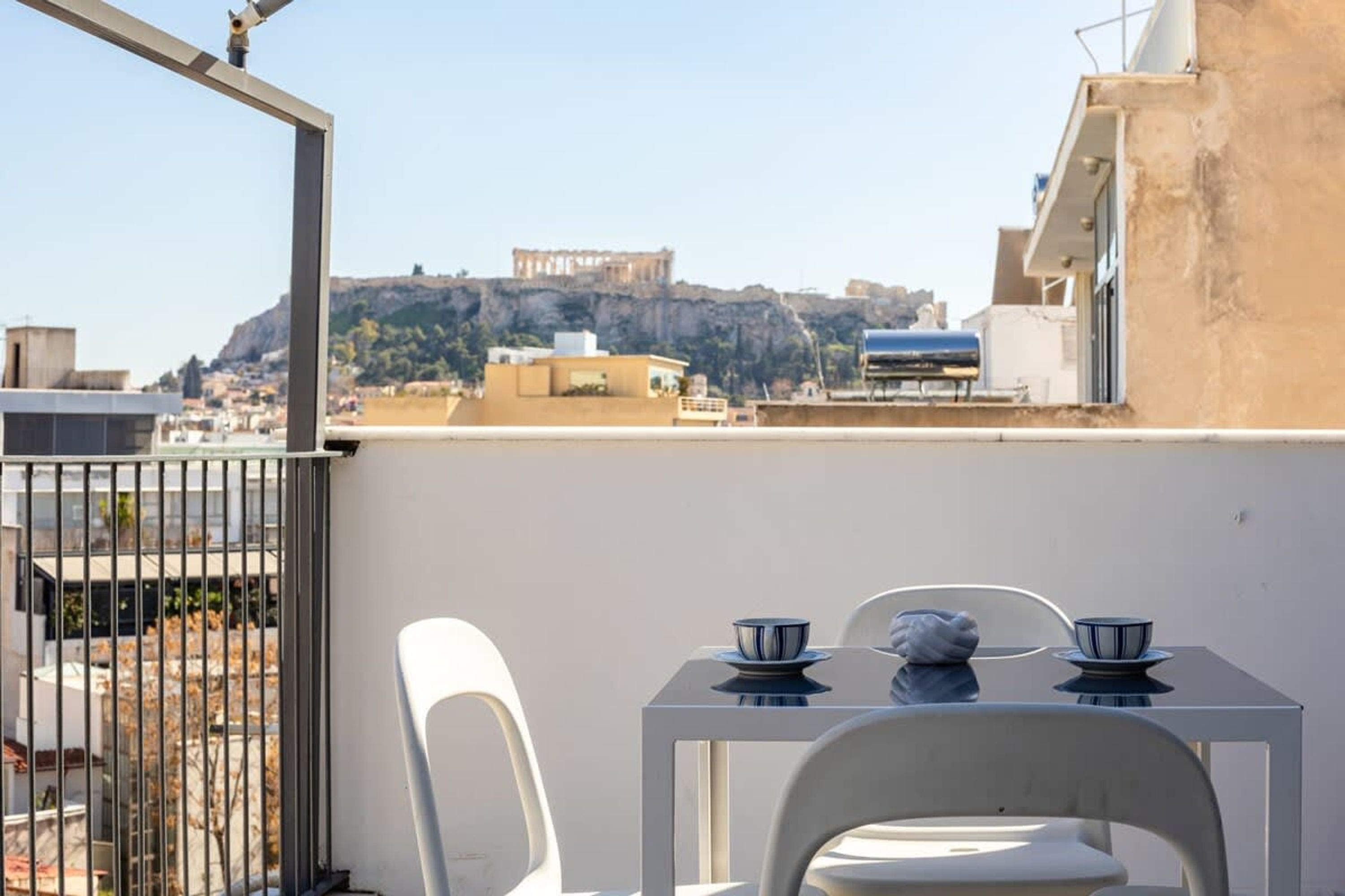 A rooftop terrace with a table and chairs, overlooking a cityscape with ancient ruins.