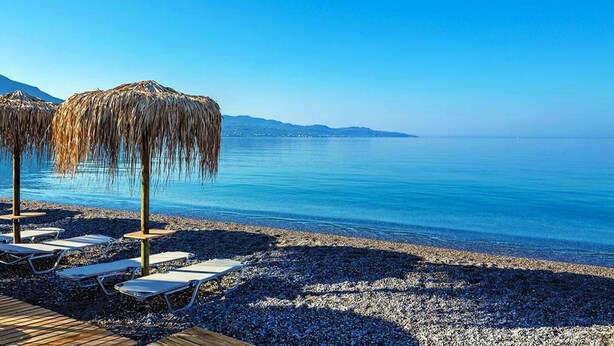 A beach with lounge chairs and thatched umbrellas, a pebble beach, and a clear view of the sea and distant mountains. - Vicky s Cozy Nest Your Home by the Sea (Kalamata)