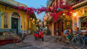 A narrow street with buildings on either side, a red scooter parked in the middle, and people sitting at outdoor tables. - Vicky s Cozy Nest Your Home by the Sea (Kalamata)