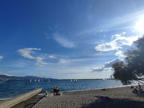 Una playa con cielo despejado, mar tranquilo y montañas a lo lejos.