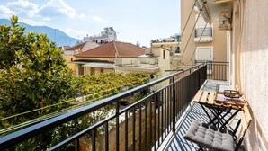 A balcony with a cushioned chair, a small table, and a hanging plant. - Vicky s Cozy Nest Your Home by the Sea (Kalamata)