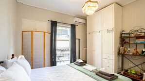 A bedroom with a bed, a wardrobe, a balcony, and a shelf with books and decorative items. - Vicky s Cozy Nest Your Home by the Sea (Kalamata)