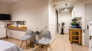 A compact living space with a kitchenette, a dining area with two chairs, a bed, and a TV mounted on the wall. - Kitries Summer Getaway - Eden Sandy Suite (West Mani)